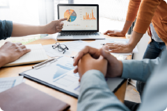 pointing at a graph on a laptop screen with others stood looking at laptop