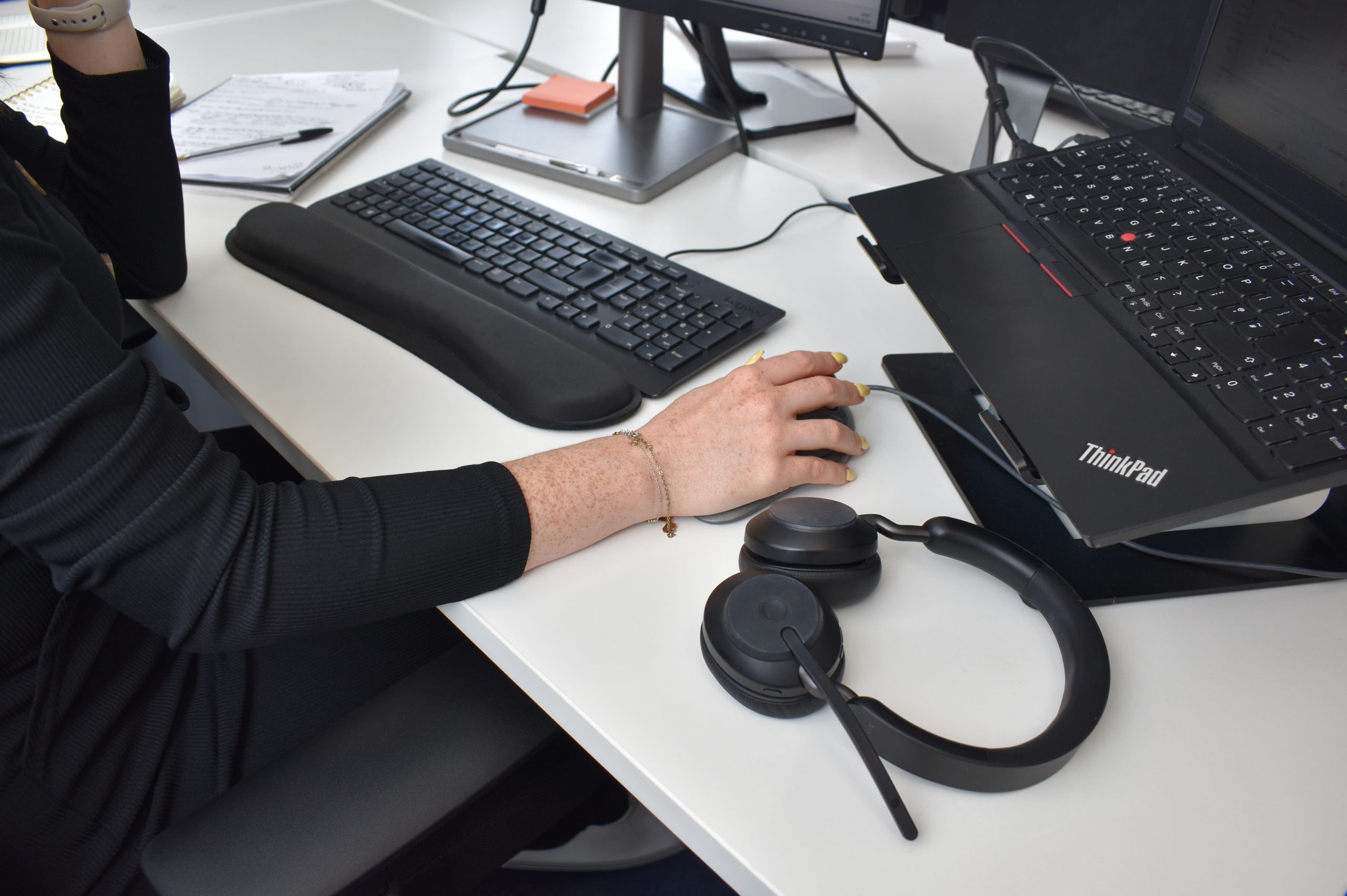 hand on a computer mouse next to a keyboard and pair of headphones